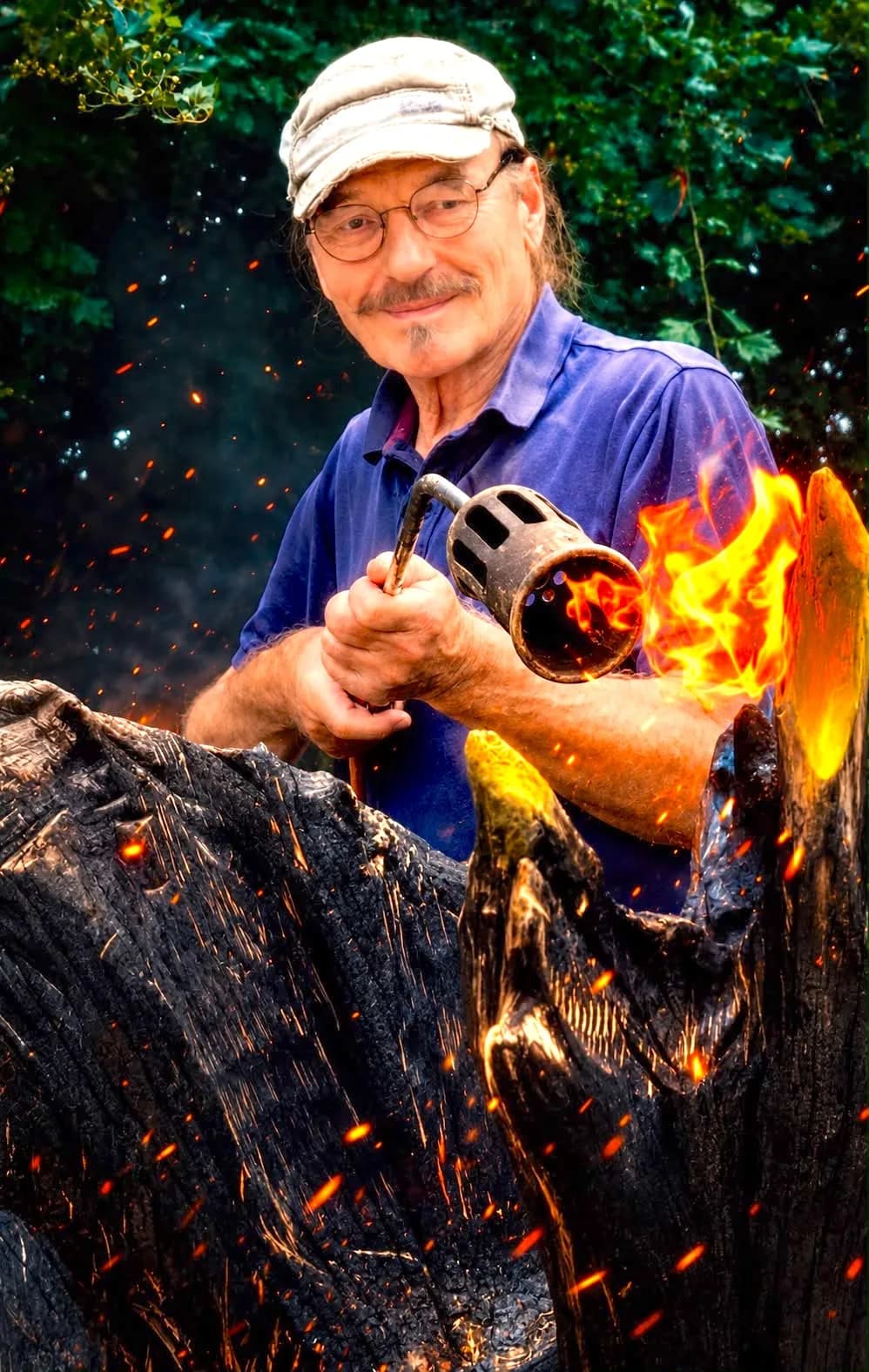 Der Künstler bei der Arbeit – eine Holzskulptur wird mit der Flamme bearbeitet, Funken fliegen.